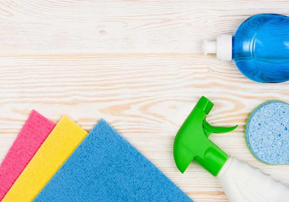 Cleaning supplies with colorful sponges, spray bottle, dish soap and scrubber on a wooden surface.