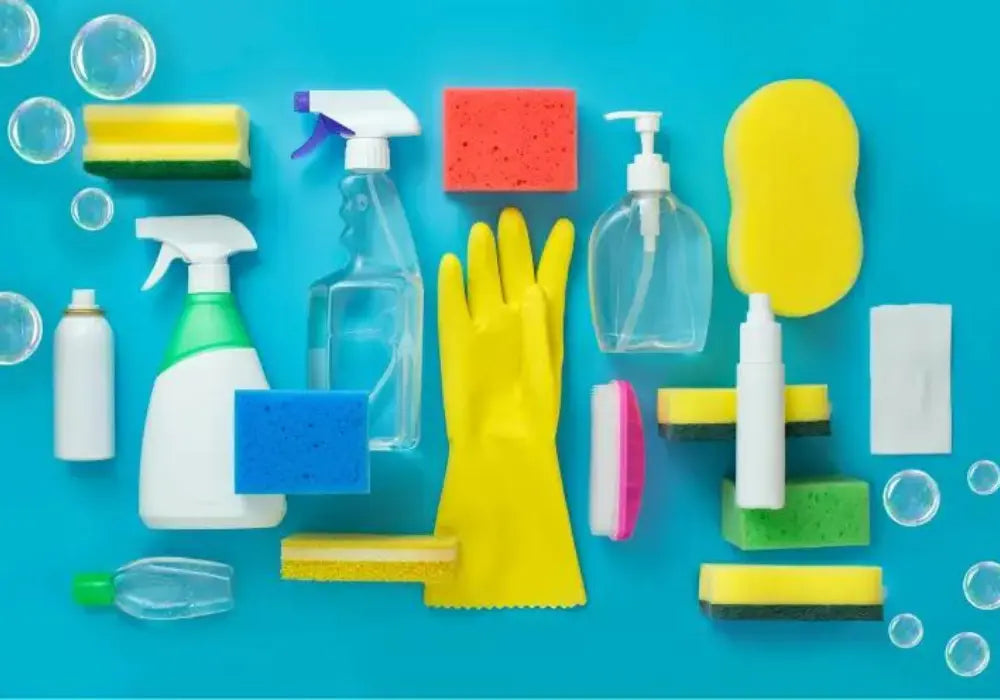 Assorted cleaning supplies, sponges, spray bottles, gloves, and soap on blue background
