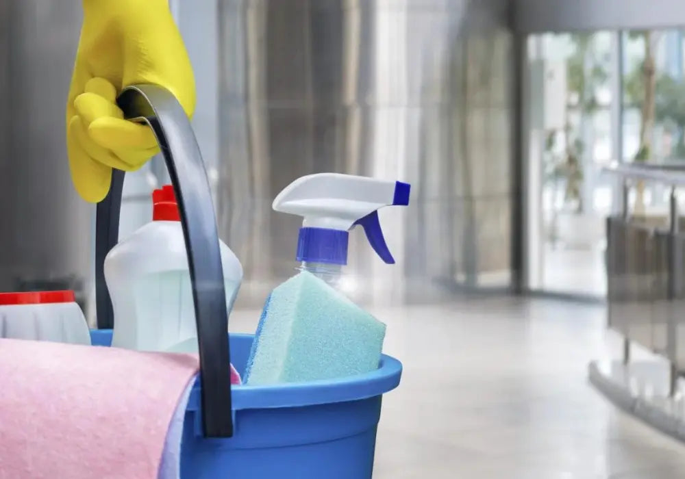 Gloved hand holding a bucket of cleaning supplies in a bright modern interior