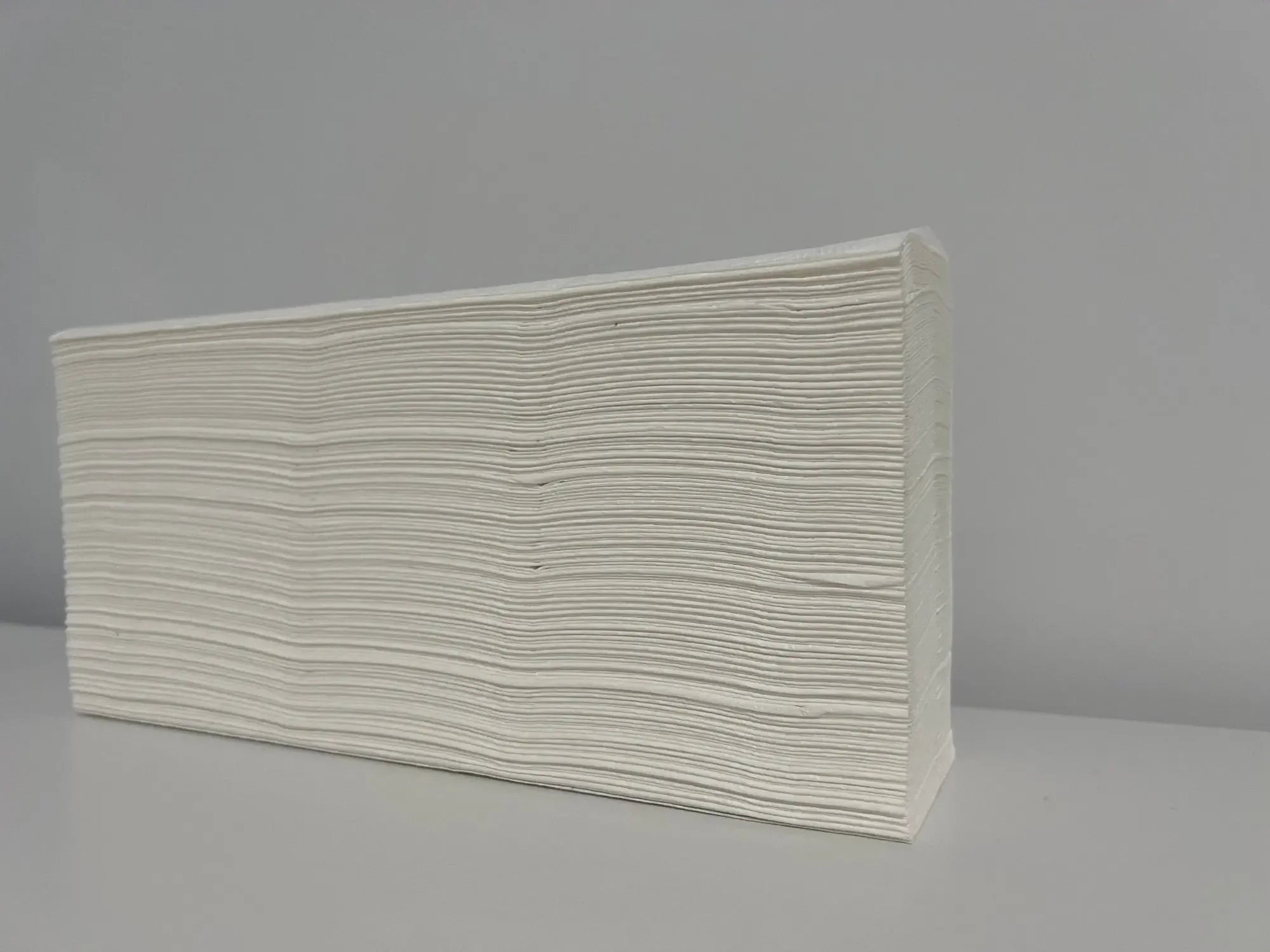 Stack of folded white paper hand towels on a plain surface for cleaning use